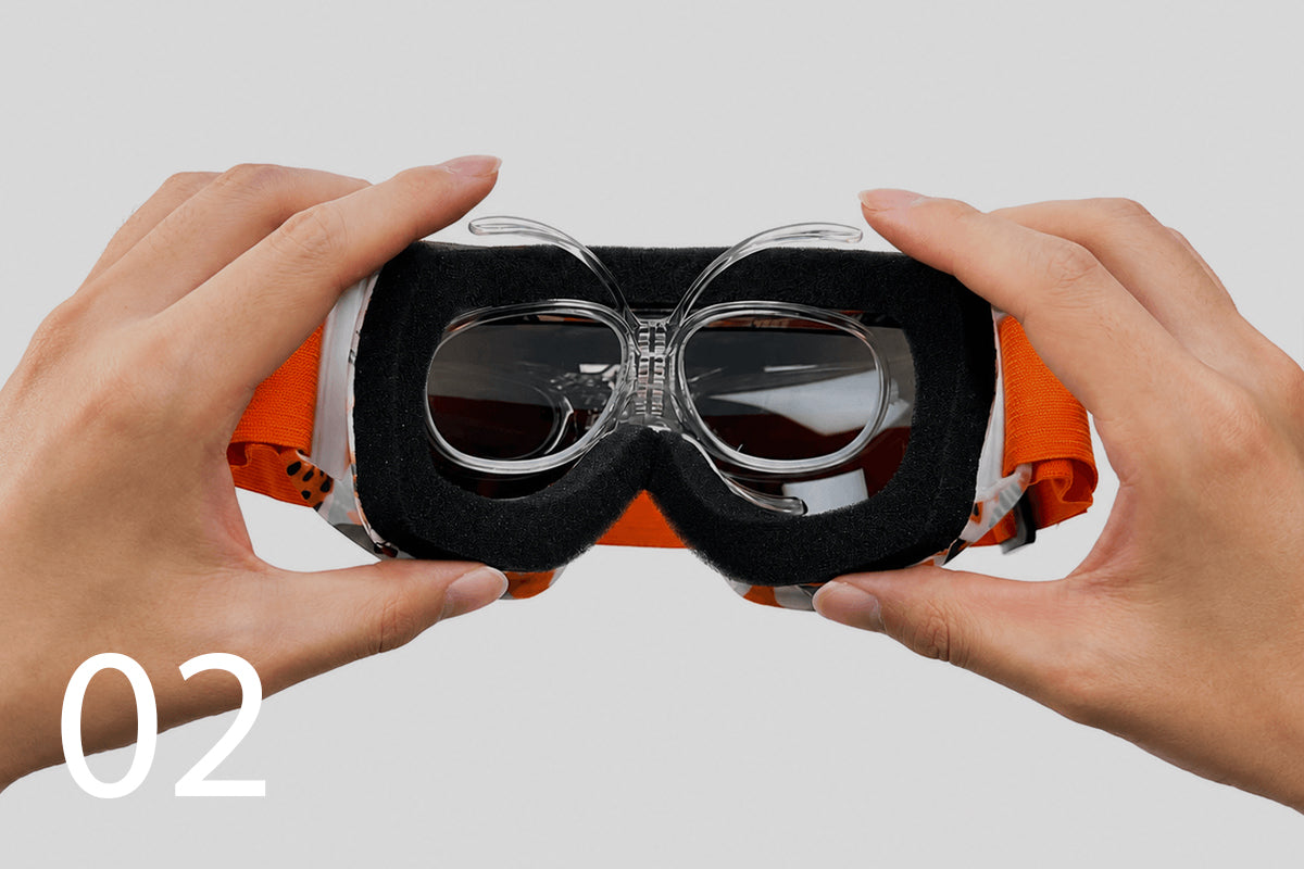 Hands positioning the clear insert inside the sports goggles.